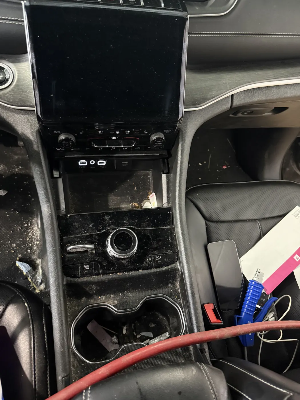 Center console with crumbs and trash in the cupholders and storage tray