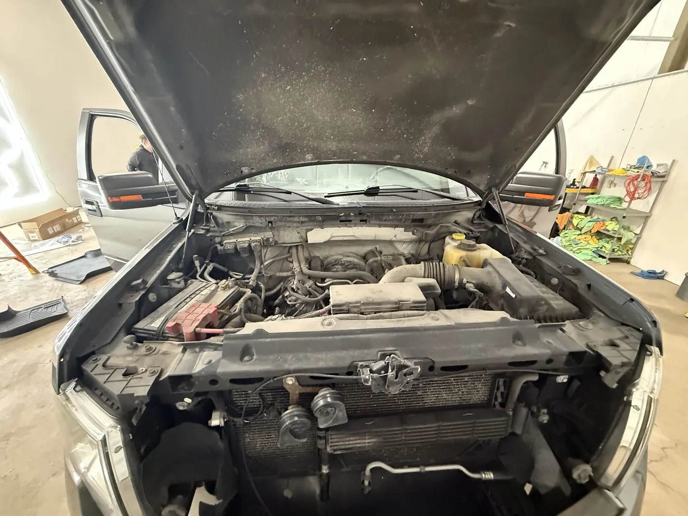 Pickup engine bay at check-in, dust caked across the engine cover and the underside of the hood