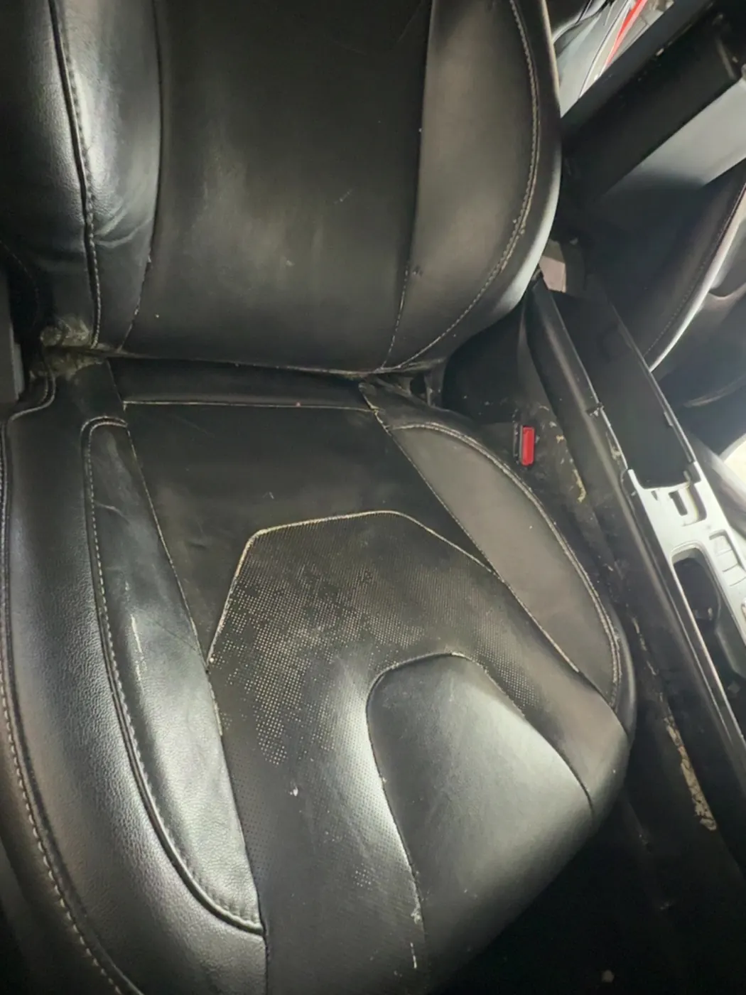 Black leather seat with grime worn into the perforations and seams