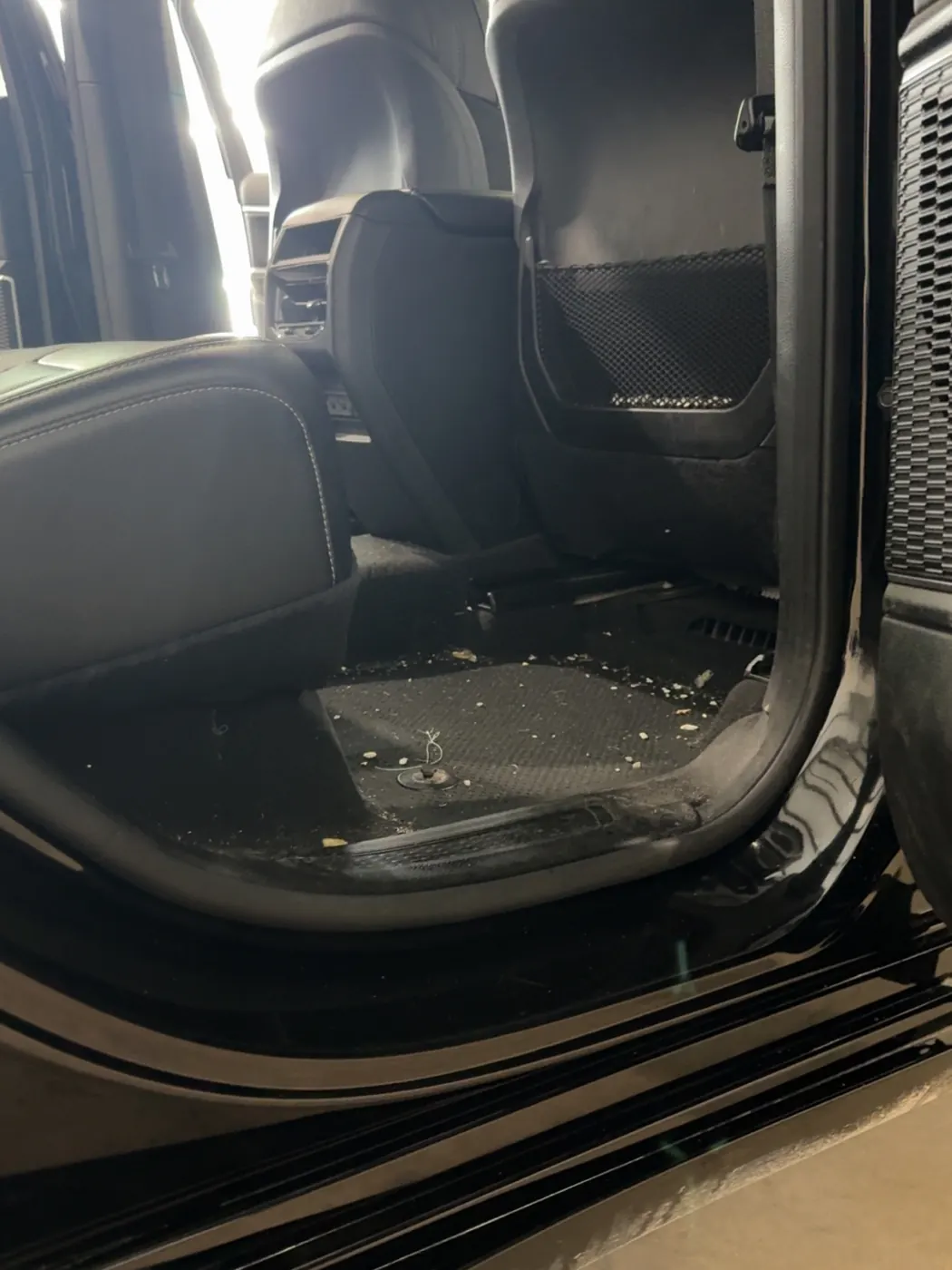 Rear footwell of a black SUV covered in crumbs and debris