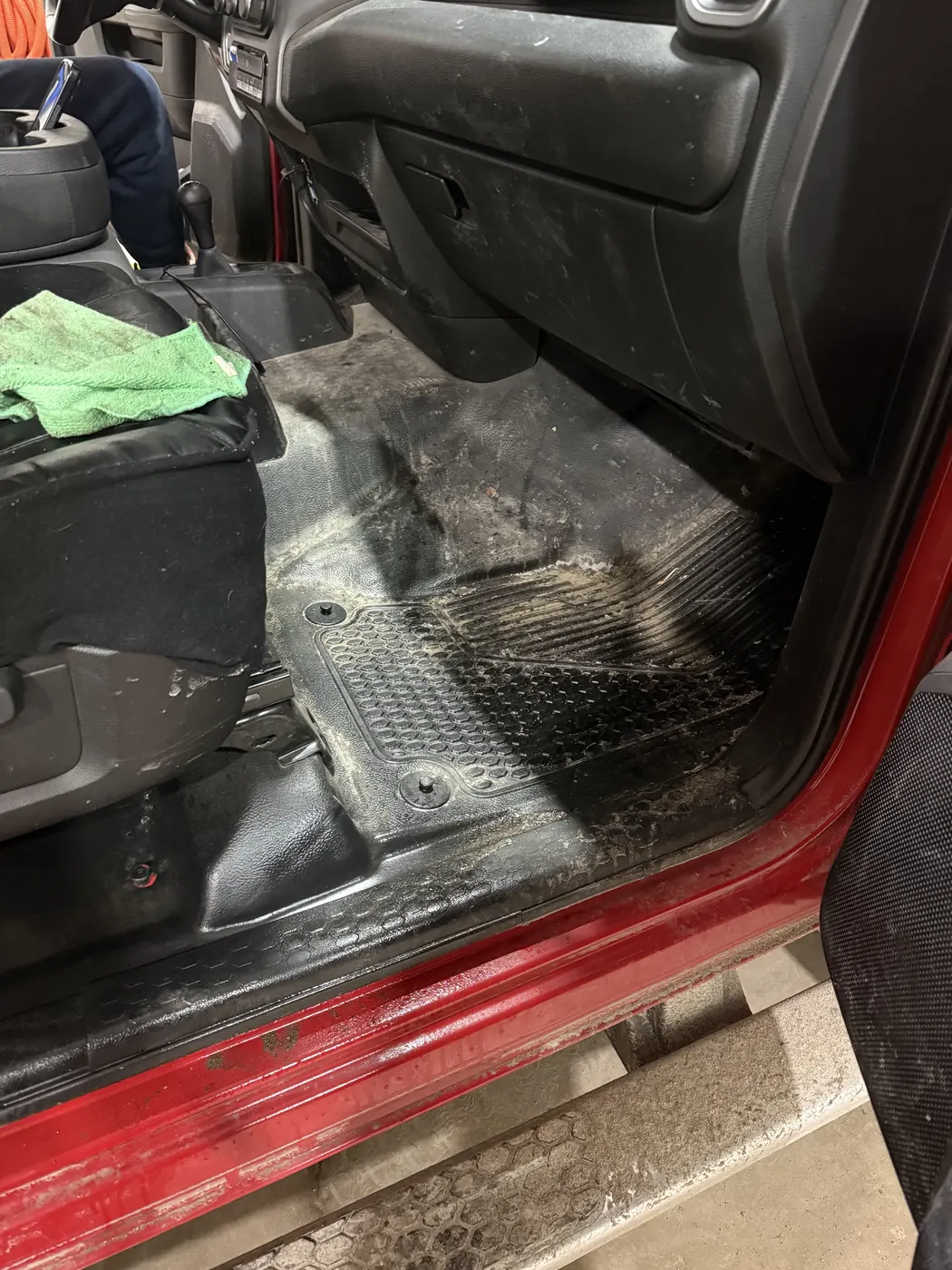 Front passenger floor of a red pickup, mud and grit ground into the liner