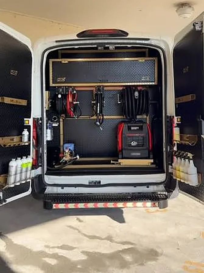 Rear doors open on a white detailing van fitted with hose reels, a pressure washer, a generator and shelves of detailing chemicals